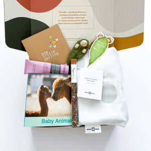 A gift hamper with organic cotton wrap, felt ornament, baby book, bergamot hand cream, Glow Tea, and Rhi Creative gift card.