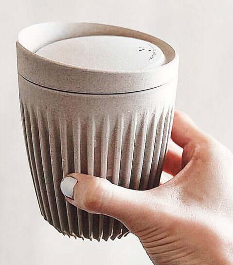 Hand holding a textured ceramic cup with a lid against a light background included in the hamper of curated with conscience
