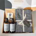 A gift box containing Australian-made hand and body products, including a herringbone patterned linen tea towel, with branding and product labels visible from curated with conscience