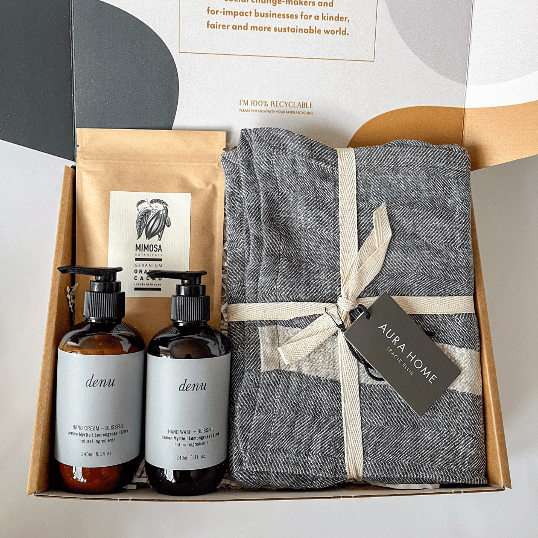 A gift box containing Australian-made hand and body products, including a herringbone patterned linen tea towel, with branding and product labels visible from curated with conscience