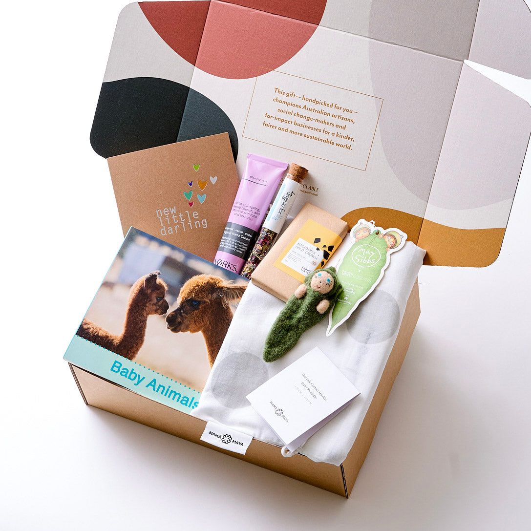 A hamper with organic cotton wrap, handcrafted baby ornament, baby animal book, plastic-free hand cream, herbal glow tea, vegan chocolate, and a recycled gift card — nurturing baby and mama.